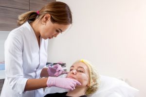 dark haired doctor pushes syringe inject into cheekbones